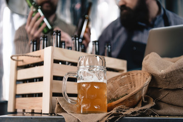 Glass of beer is on table on background of two men picking up bottle. Still life with glass of beer.
