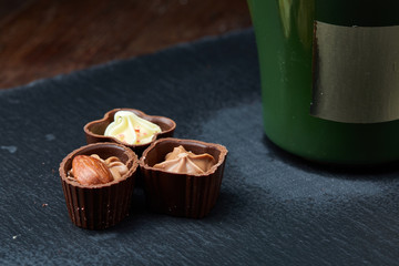 Three chocolate candies and coffee cup on stone board over wooden background, selective focus, close-up