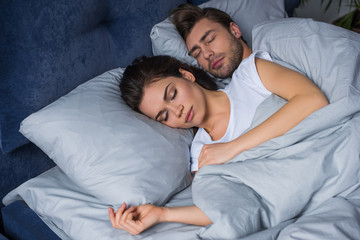Young attractive couple hugging while sleeping in bed