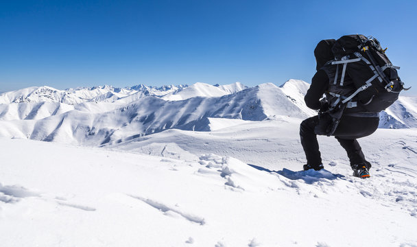 Wanderer with a backpack crouched down and admires mountain snow-capped peaks.