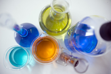 various chemical bottles and graduated tube filled with colored liquids, view from above

