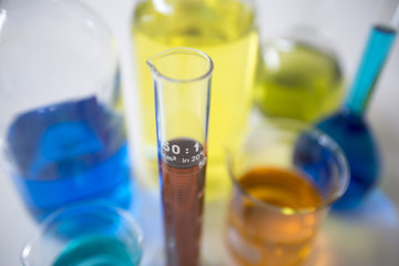 various chemical bottles and graduated tube filled with colored liquids, view from above
