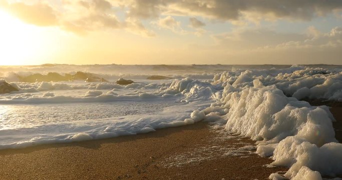 Vague d'&eacute;cume de mer sur la plage au coucher du soleil