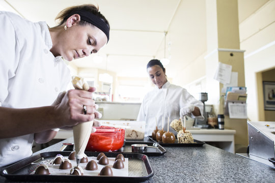 Caucasian woman and Hispanic woman working on creating candy in a candy shop.