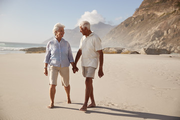 Senior Retired Couple Walking Along Beach Hand In Hand Together