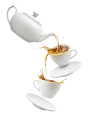 teapot pouring tea into flying cups, on white background