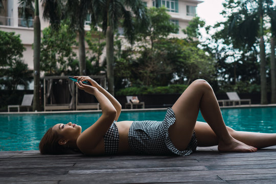 Side view of woman using smartphone while relaxing at pool