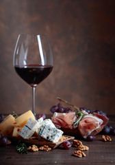 Glass of red wine with various cheeses , fruits and prosciutto .