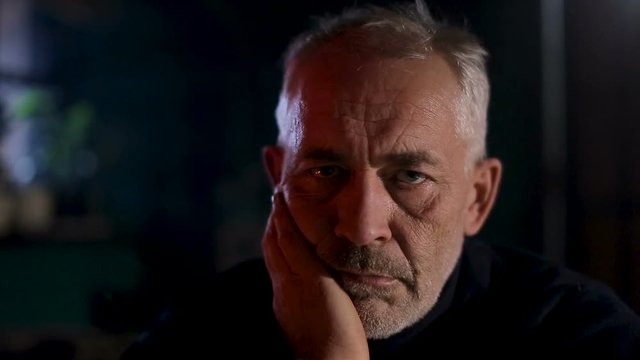 Senior old man sitting by the fireplace with sad thoughtfull expression