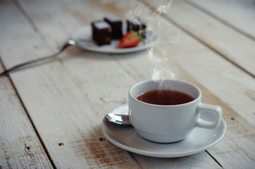 hot coffee in white cup with steam on wood table with cake.