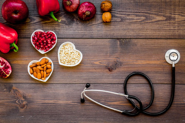 Products good for heart and blood vessels. Vegetables, fruits, nuts in heart shaped bowl near stethoscope on dark wooden background top view copy space