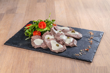 boiled beef tongue with sauce, capers and greens on a black granite tile