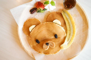 Cute pancake. Kids menu of teddy bear pancake served with fresh cream, strawberry, banana and maple syrup. Creative food art concept.