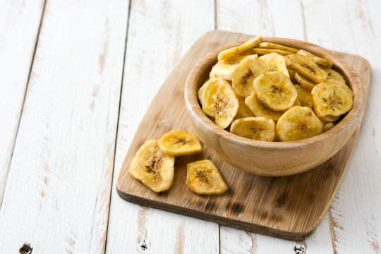 Banana chips in bowl on white wooden table. Copyspace