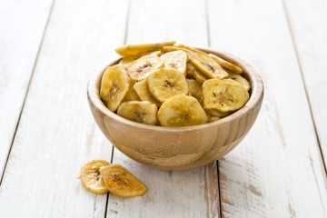 Banana chips in bowl on white wooden table.