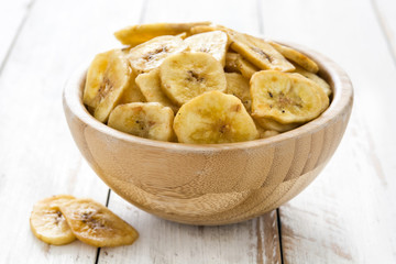 Banana chips in bowl on white wooden table.