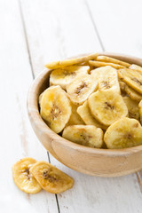 Banana chips in bowl on white wooden table.