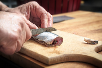 male hands preparing a herring fish with a kitchen knife on a wooden cutting board,  copy space