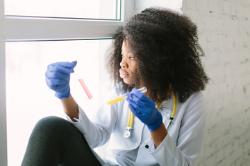 Young beautiful African American girl doctor in a white coat with a stethoscope. sitting at a table...