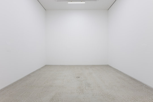 A view of a white painted interior of an empty room or an art gallery with a fluorescent lighting and concrete floors