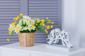 Yellow bouquet in a wicker basket is on the table by the window. Spring flower arrangement in the interior. Symbol of love.