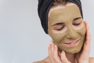 Closeup cropped portrait of young woman applying clay mask on clean face doing beauty wellness treatment on her face skin. Horizontal shot of female applying organic facial mask, with closed eyes.