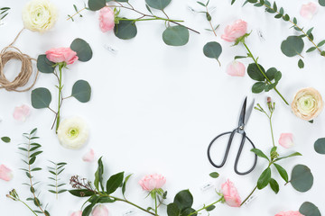 Top view of frame wreath flower pattern with roses, eucalyptus leaves, branches, notebook, scissors, jute tape isolated on white background, flat lay