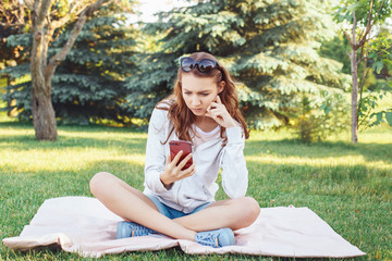 Portrait of young worried Caucasian teenage girl with her phone outside in park. Serious stressed woman with mobile cell phone