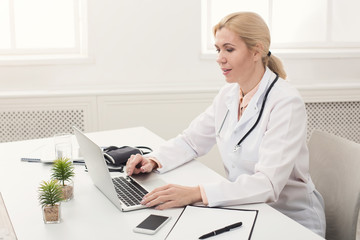 Serious female doctor typing on laptop