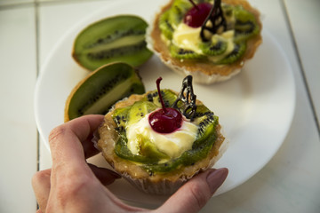 A female hand holds delicious fruit cake with curd cream with kiwi and cherry