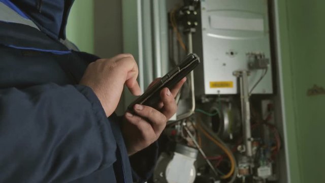 Worker typing on smartphone against gas-fire boiler 