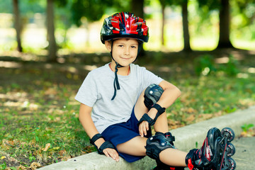 Little boy riding on rollers in the summer in the Park. Happy child in helmet learning to skate.