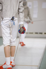 Rear view of teenage fencer in white clothes on the fencing tournament