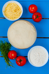 Pizza dough with ingredients on blue wooden table.