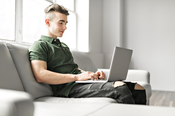 Handsome man using a laptop sitting on couch at home