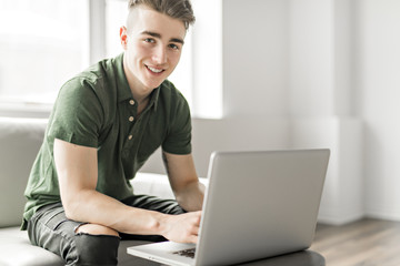 Handsome man using a laptop sitting on couch at home