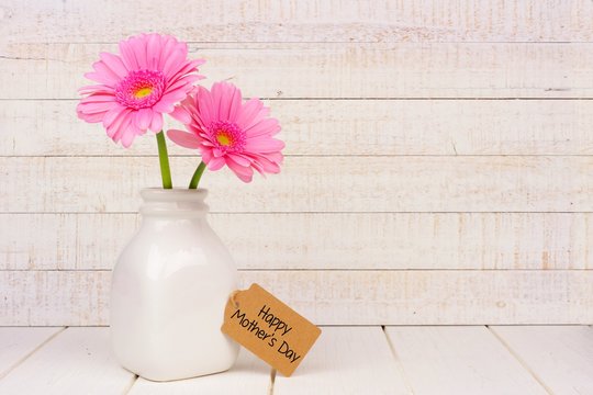 Happy Mothers Day gift tag with vase of pink flowers against a rustic white wood background