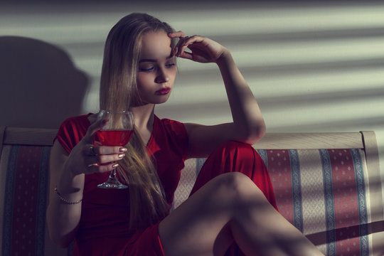Portrait of beautiful young woman with glass of red wine and the shadows from the blinds.