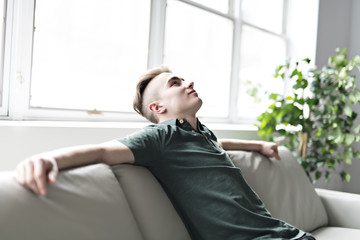 Young man sitting on coach rest at home