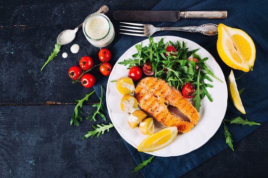 Grilled Salmon With Arugula And Cherry Tomato Salad And Potatoes On Blue Background