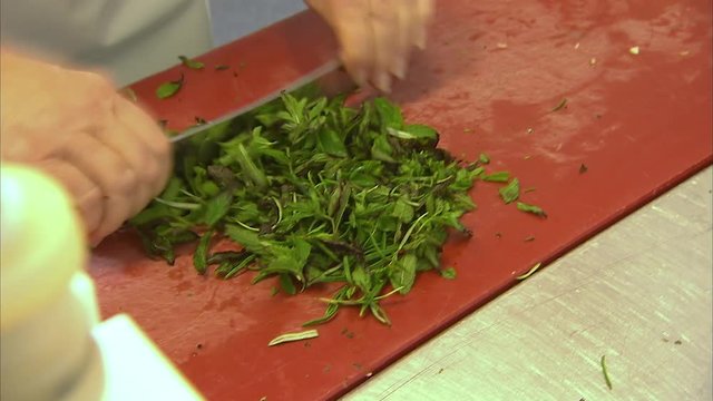 A tracking medium shot of two chef as they chop garlic and parsley.