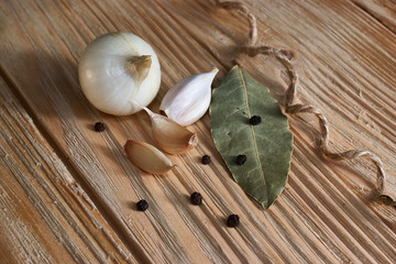 On the wooden table, seasonings: onion, garlic, black pepper peas and bay leaf
