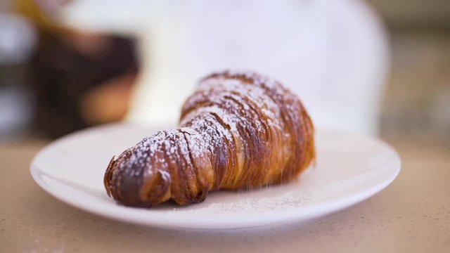 the cook sprinkles a croissant with powdered sugar.