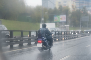 A man riding his scooter in the rain, a lifestyle of people living in urban area. road with metal safety rail - 198228196