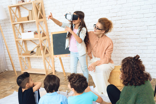 Cute girl looks into virtual reality glasses at classroom of elementary school.