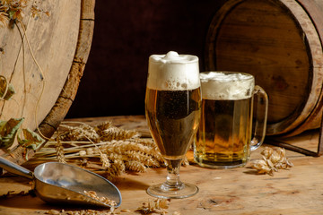 Beer glass, old barrel, dried hops and wheat ears on wooden table. Dark background.