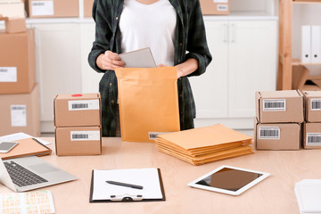 Young woman preparing parcel envelopes for shipment to client in home office
