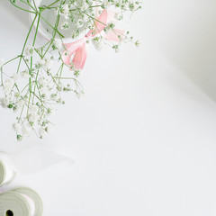 Soft background with white gypsophila, pink ribbon, wooden spool with silk ribbon. Top view