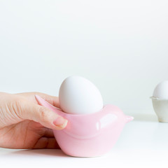 Girl's hand with white egg in pink birdie egg stand