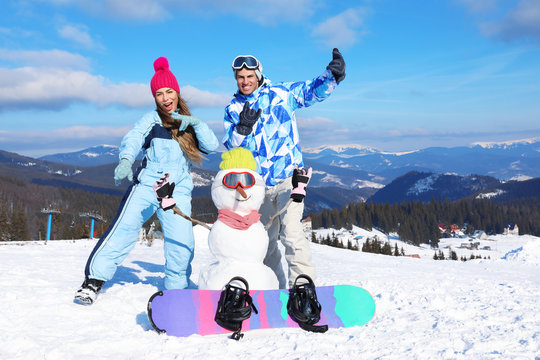 Happy couple with snowman having fun at ski resort. Winter vacation